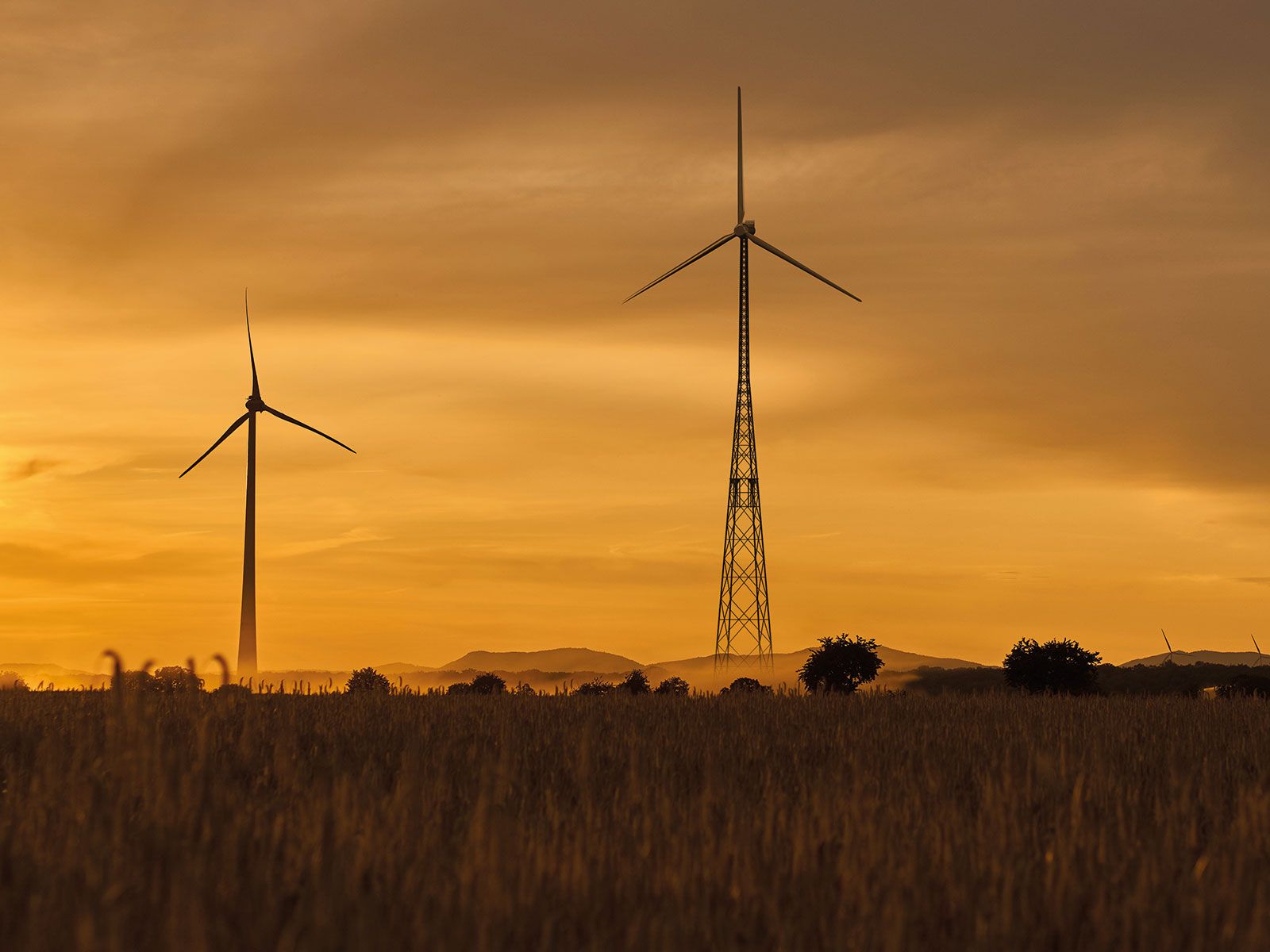 Two wind turbines in a hilly landscape at sunset