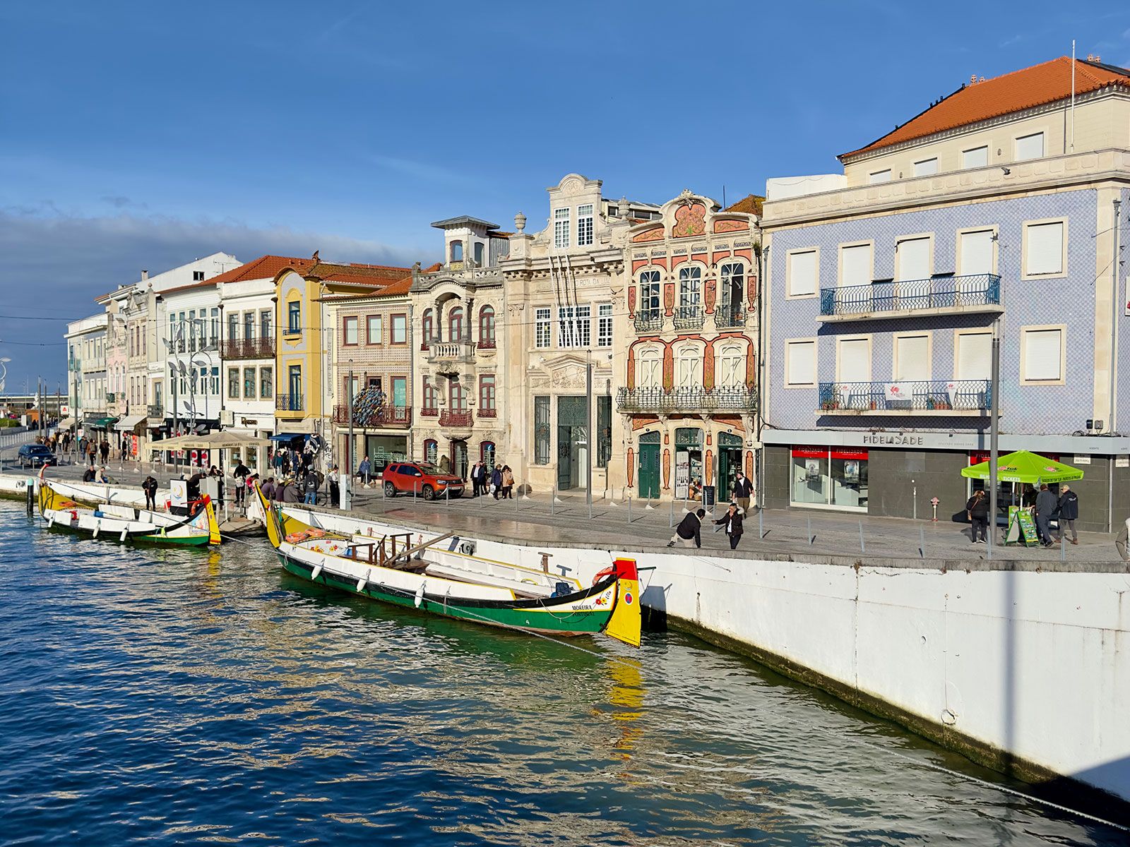 Bunte Häuserzeile am Kanal in Aveiro, Portugal, mit traditionellen Moliceiro-Booten, die am Ufer vor dekorativen Jugendstil-Fassaden liegen.