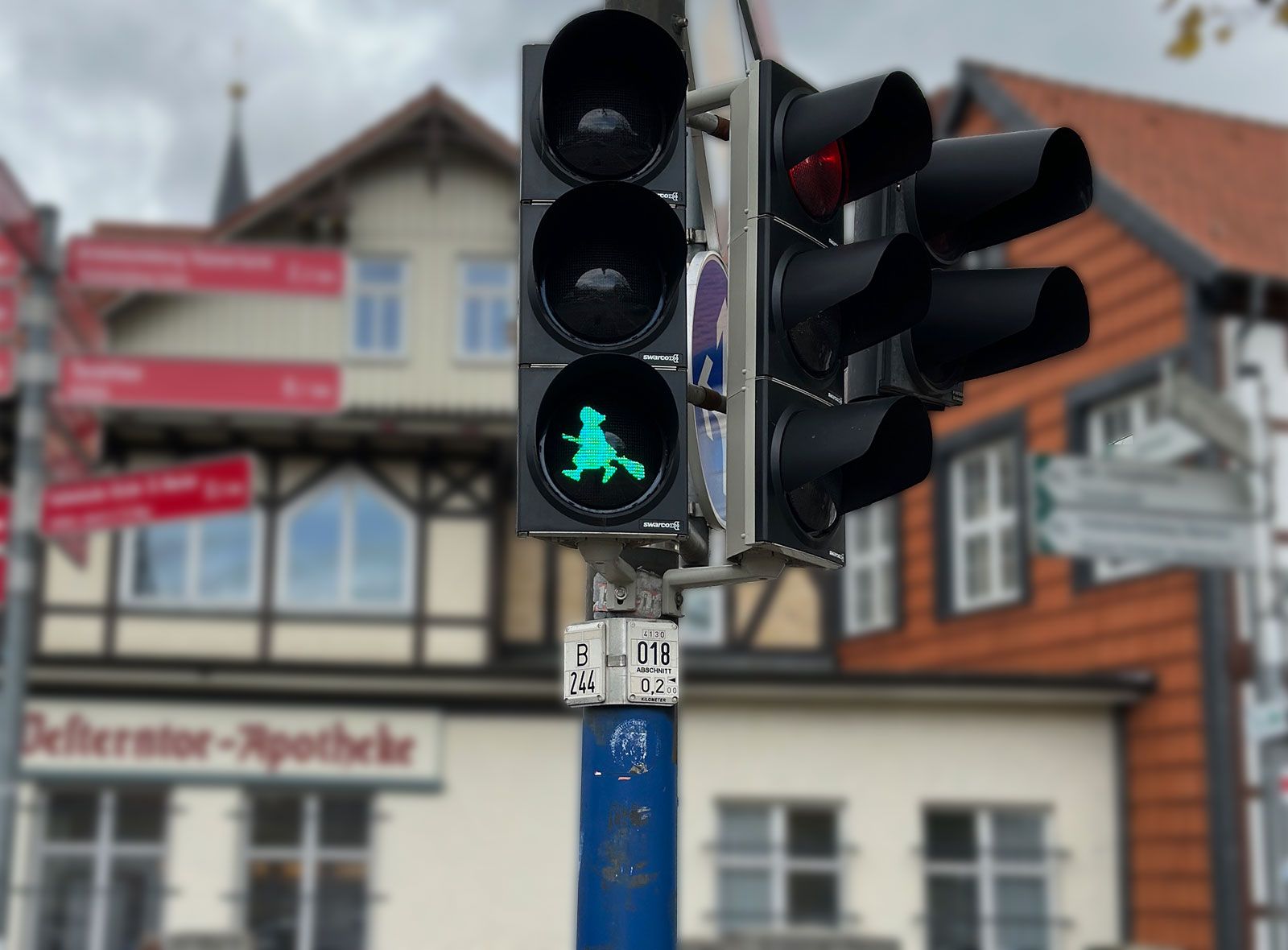 A pedestrian traffic light shows a green illuminated symbol in the shape of a flying witch on a broomstick.