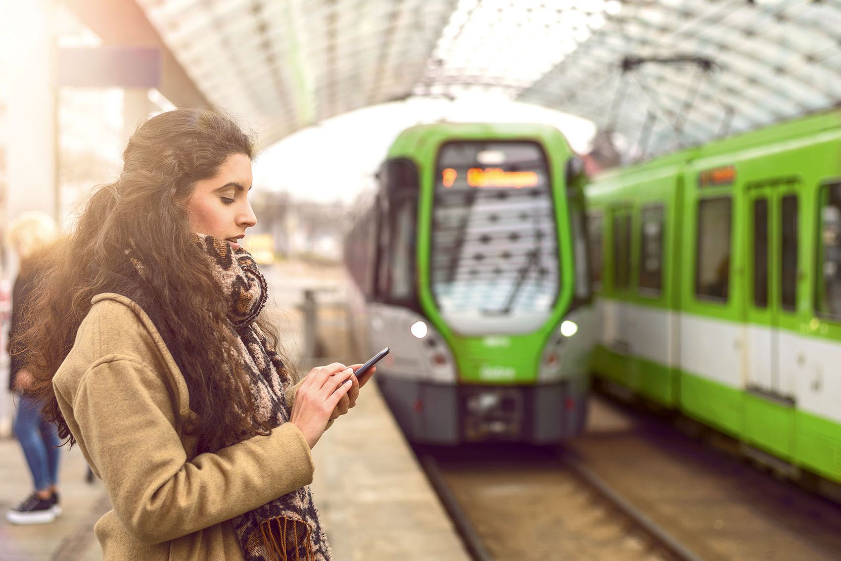 A woman is waiting on the platform for a train and, in the meantime, looking at her smartphone.