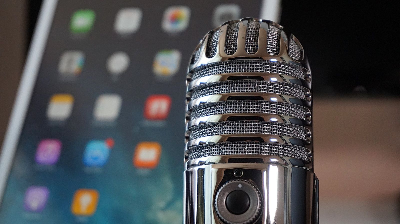 Close-up of a silver microphone, with the screen of an iPhone visible in the background.